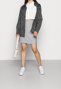 Grå kort jacka över en vit blus, kombinerad med en åtsittande grå kjol och vita sneakers. Accessoarer med en flätad vit handväska.