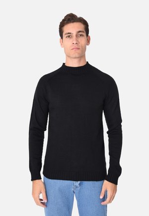 Maglione nero a maglia con colletto a girocollo alto, maniche lunghe, polsini a coste e orlo dritto, indossato sopra jeans blu.