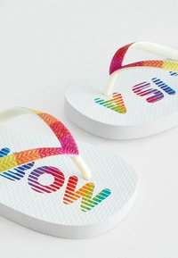 Tongs blanches avec des semelles texturées. Bretelles dégradées colorées arborant le texte "WOW" en rayures arc-en-ciel. Matériau lisse et flexible.