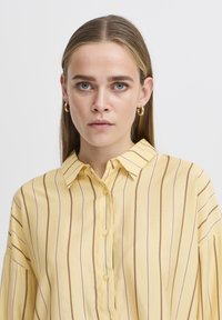 Blusa gialla a righe realizzata in tessuto leggero, con colletto, chiusura con bottoni e dettagli plissettati sulle maniche.