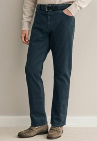 Pantalones de mezclilla oscura con un corte de pierna recta, que cuentan con un clásico cierre de botón y cremallera, y un cinturón de cuero negro. Textura suave.