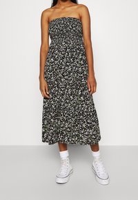 Svart blommig strapless klänning med en samlad midja, utsvängd kjol och vita högskaftade sneakers med ihoprullade strumpor.