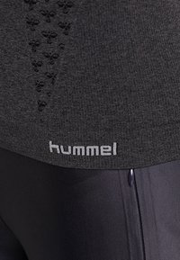 Top atletico grigio con un design testurizzato e piccoli modelli neri, marchiato "hummel" sull'orlo, abbinato a leggings neri eleganti.