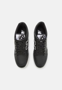 Czarne buty sportowe z cholewką ze skóry, perforowanym wzorem, czarnymi sznurówkami i białym logo na języku. Gumowa podeszwa zapewniająca przyczepność.