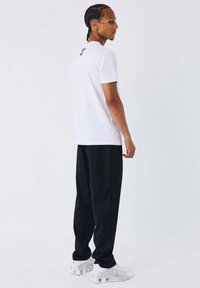 T-shirt bianco a maniche corte con un logo nero sulla parte posteriore, abbinato a pantaloni neri larghi e scarpe da ginnastica bianche.