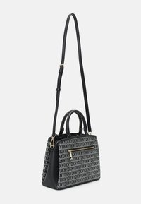 Sac à main DKNY noir et gris avec logo imprimé, poche zippée dorée, double poignée et longue bandoulière réglable sur fond blanc.