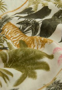 Tissu avec imprimé tropical montrant des feuilles de palmier vertes, de grandes feuilles noires et marron, ainsi qu'un motif tigre jaune sur fond crème.