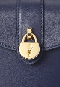 Σακούλα από ναυτικό δέρμα με χρυσό κλείσιμο και χαρακωμένα αρχικά, λεία υφή και ορατές ραφές κατά μήκος των ακρών.