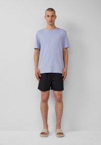 Licht lavendel kleurig T-shirt met korte mouwen, zwarte shorts en beige slippers. De stof lijkt lichtgewicht, met een ontspannen pasvorm en een eenvoudig ontwerp.