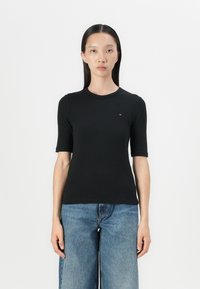 Zwarte geribbelde t-shirt met een ronde hals, korte mouwen en een klein logo op de borst. Combi met blauwe wijde denim jeans.