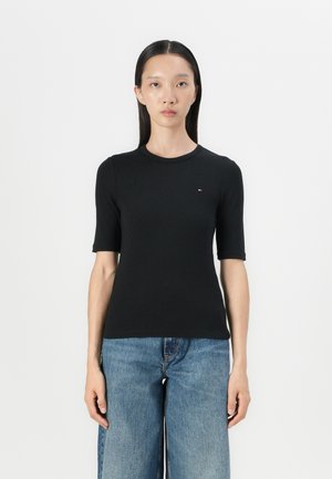Zwarte geribbelde t-shirt met een ronde hals, korte mouwen en een klein logo op de borst. Combi met blauwe wijde denim jeans.