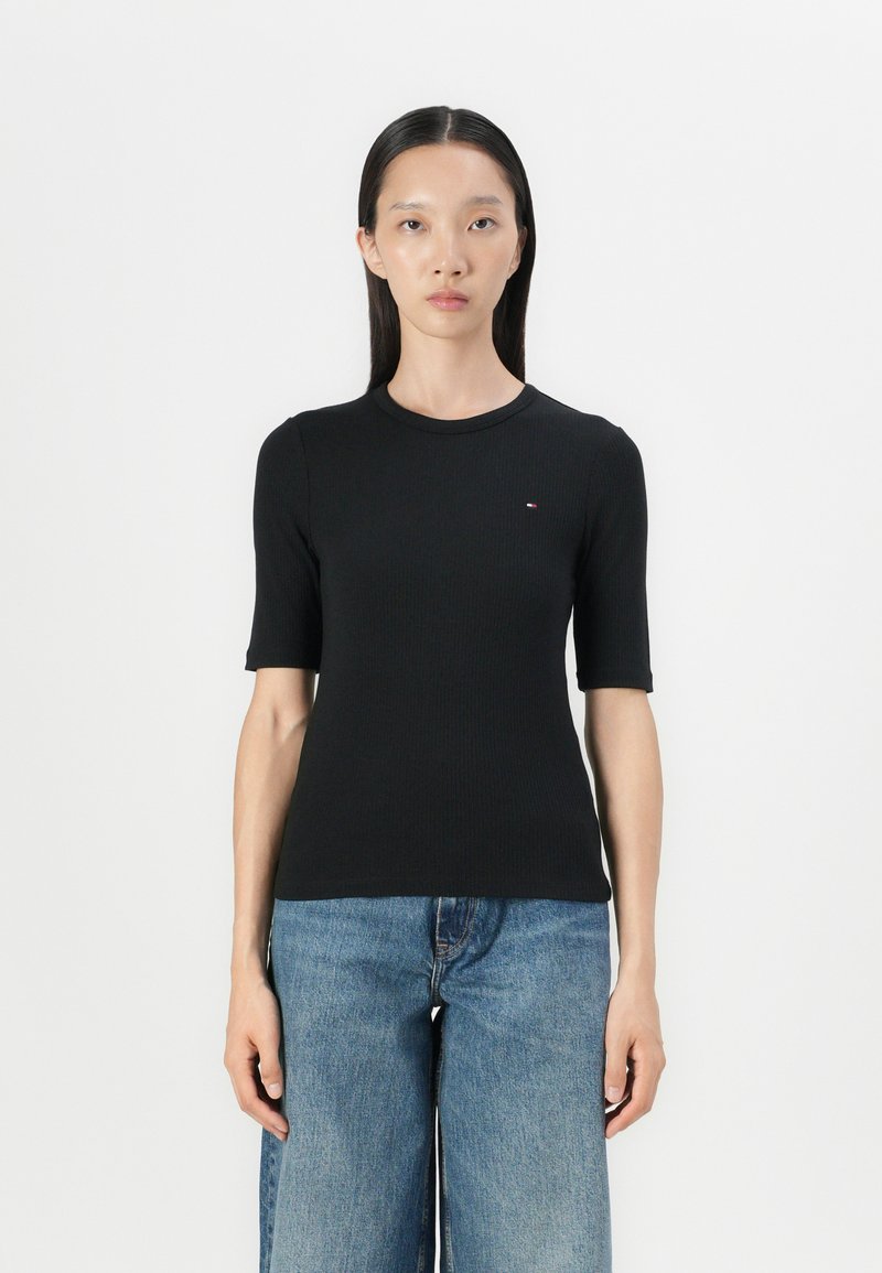 Zwarte geribbelde t-shirt met een ronde hals, korte mouwen en een klein logo op de borst. Combi met blauwe wijde denim jeans.
