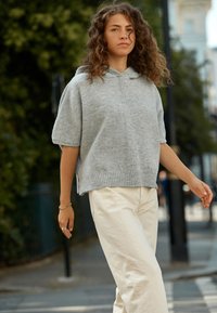 Világosszürke, rövid ujjú kapucnis pulóver puha anyagból, bordázott szegéllyel és kényelmes szabással, krémszínű, széles szárú nadrággal párosítva.