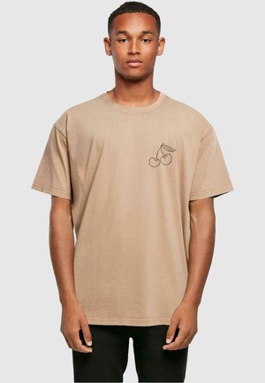 Beige bomull t-skjorte med korte ermer, med en svart brodert kirsebærdesign på venstre bryst og en avslappet passform.