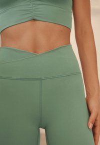 Lichtgroene crop top en hoge taille legging gemaakt van gladde stof, met een kruisvormig tailleontwerp en zichtbare stiksel details.