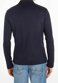 Marinblå långärmad polo med krage och en mjuk textur, ihopparad med ljusblå jeans med synliga bakfickor.