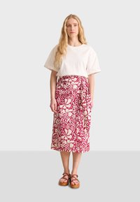 T-shirt bianco in cotone abbinato a una lunga gonna avvolgente con un motivo floreale rosa e crema; sandali con platform marroni completano il look.