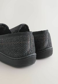 Papuci gri din material moale cu talpă din cauciuc negru. Prezintă o suprafață texturată și un subtil model cu carouri portocalii. Margini rotunjite și confortabile în design.