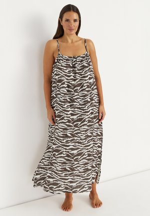 Kvinde står barfodet iført en løs, ærmeløs kjole i ankel-længde med sorte og hvide abstrakte zebra-striber.