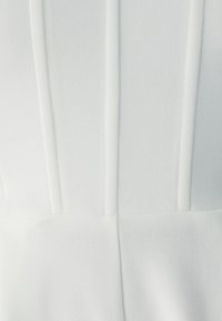 Witte kleding met verticale naden, een gladde stofstructuur en een nauwsluitend ontwerp, met de nadruk op strakke lijnen en minimale details.
