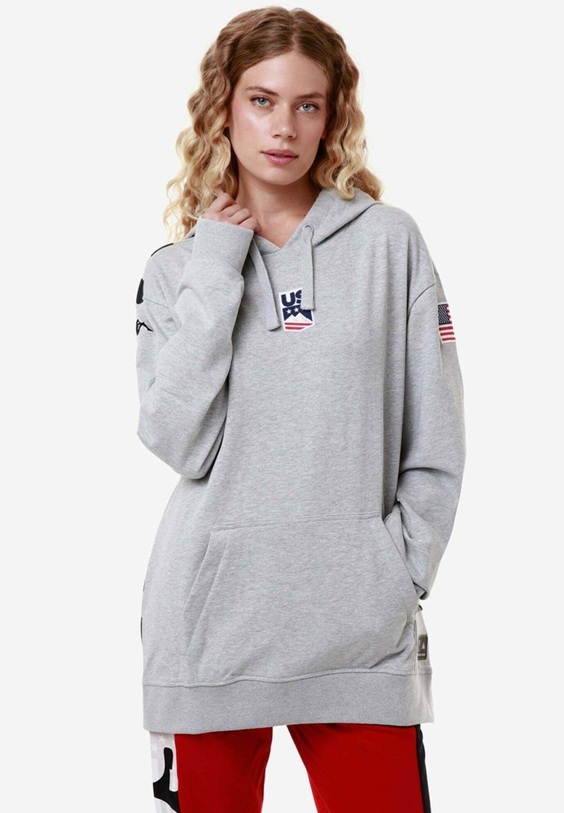Felpa grigia con tasca davanti, presenta un logo "US" con stelle e una patch della bandiera americana su una manica. Tessuto morbido, vestibilità rilassata.