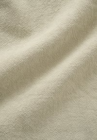 Beige woven fabric with a subtle textured pattern and soft folds creating light shadows and depth.
