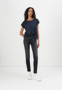 Haut à manches courtes bleu marine avec une poche, associé à un jean en denim noir ajusté et des baskets blanches. Texture lisse et design décontracté.