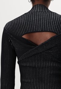 Svart ribbat långärmad topp med silvertrådar, med en hög halsringning och en öppen ryggdesign med korsade tygdetaljer.