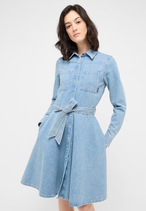 Jeanskleid in Hellblau mit langen Ärmeln, Knopfleiste vorne, zwei Brusttaschen und einem passenden Gürtel, der die Taille betont. Ausgestellter Rock.