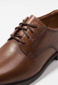 Braune Leder-Halbschuhe mit Schnürung, glatter Oberfläche, dezenten Stickdetails und runder Zehenpartie. Schwarze Gummisohle.