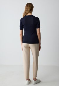 Top blu navy a maniche corte con collo a costine, abbinato a pantaloni beige chiaro a sigaretta e sneaker bianche. Tessuto morbido e design aderente.