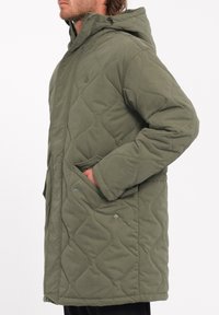 Gequilted olijfgroene jas met capuchon, voorzien van drukknoopzakken, een relaxed fit en textuurpatronen op het oppervlak van de stof.
