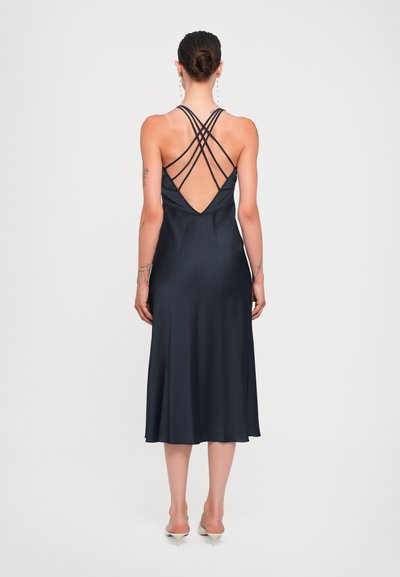 Marine satijnen slipdress met een diepe V-rug, voorzien van gekruiste banden. De zoom reikt tot halverwege de kuit en benadrukt de gladde textuur en het elegante ontwerp.