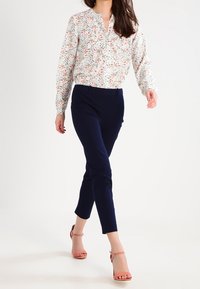 Kukkakuvioinen vaaleampi paita, tummansiniset istuvat housut ja vaaleanpunaiset remmisandaalit. Paidassa on napitus edessä ja käärityt hihat.