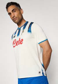 Witte voetbalshirt met korte mouwen, voorzien van zwarte en blauwe verticale strepen en een opvallend rood 'Cete' logo. Gestructureerde stof met blauwe accentdetails.
