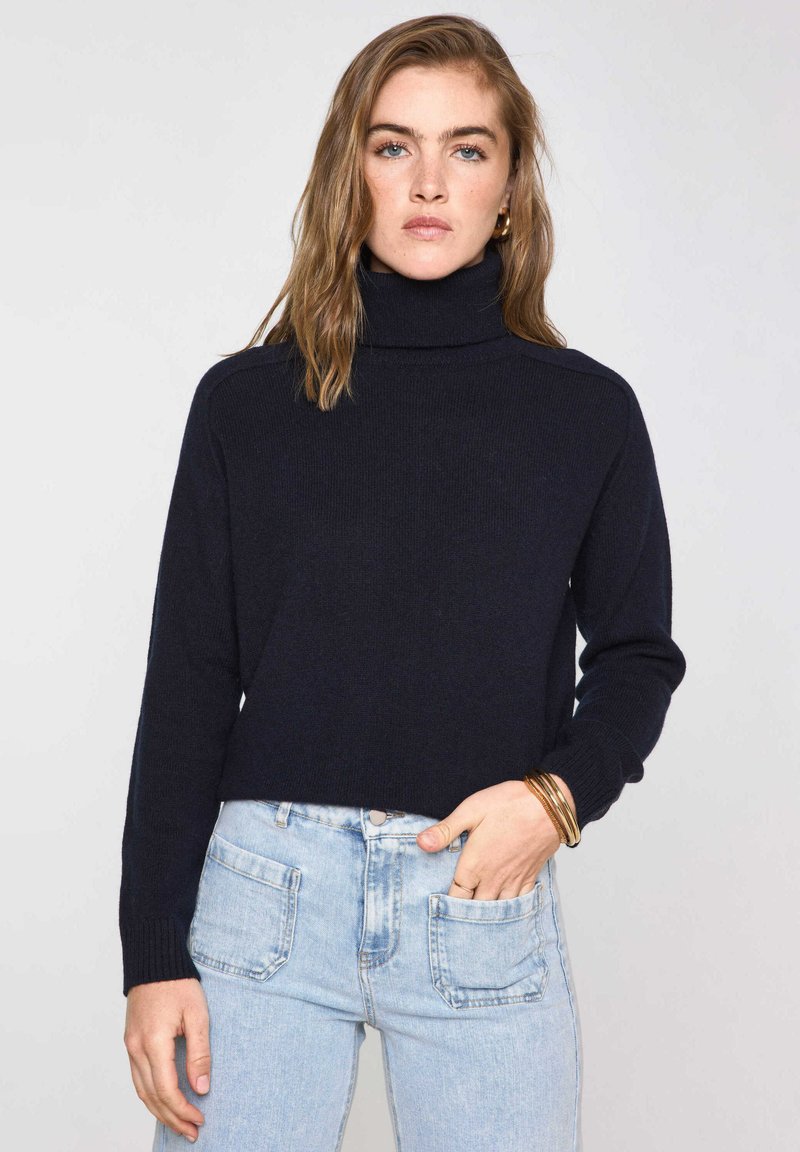 Maglione a collo alto blu navy in morbido tessuto a maglia, con design corto, polsini a costine e silhouette rilassata, abbinato a jeans azzurri.