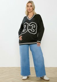 Mustat neulotut v-aukkoiset villapaidat, joissa on valkoiset raidat ja numero 93. Yhdistetty vaaleansinisiin leveisiin farkkuihin ja valkoisiin lenkkareihin.