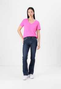 Tricou roz deschis cu decolteu în V, purtat cu blugi negri și adidași albi, având un croi lejer și mâneci scurte.