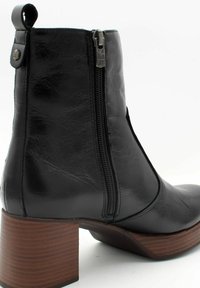Botte chelsea en cuir noir avec une fermeture éclair sur le côté, bout rond et un talon en bois empilé. Texture lisse avec une légère brillance.