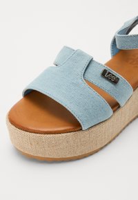 Sandal com plataforma de lona azul claro, com duas tiras largas, palmilha de couro castanho e sola de plataforma em juta bege texturizada. Acento de logótipo em metal.
