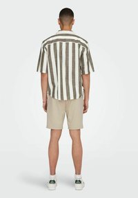 Kortærmet stribet skjorte i beige og brun med en afslappet pasform, et par beige shorts og hvide sko med grønne detaljer. Bagansigt.