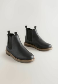 Czarne skórzane botki za kostkę z elastycznymi panelami po bokach, o fakturowanym wykończeniu, zaokrąglonym nosku oraz solidnej brązowej podeszwie. Pasują do różnych stylizacji.