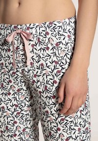 Witte pyjamabroek met een bloemig patroon in roze en zwart; voorzien van een elastische tailleband en een roze trekkoord.