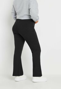 Mustat levenevät housut, jotka on valmistettu pehmeästä materiaalista, ja joissa on sileä pinta sekä tiukka muotoilu, yhdistettyinä valkoisiin tennareihin.