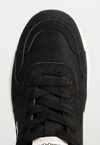 Bout de basket noir avec des détails en mesh et en daim, lacets noirs noués, et une partie de la semelle blanche visible en bas.