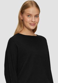 Schwarzer, strukturierten Pullover mit horizontalem Rippmuster, weitem Ausschnitt und langen Ärmeln, vor einem neutralen Hintergrund präsentiert.