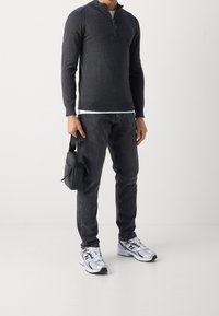 Maglione zip grigio scuro con maniche lunghe, abbinato a jeans neri e t-shirt bianca. Sneakers grigie e nere. Borsa a tracolla nera.