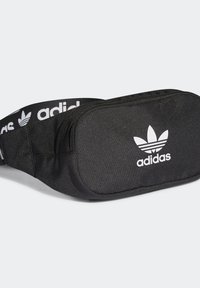 Mustapaitainen vyölaukku, joka on valmistettu teksturoidusta kankaasta. Siinä on vetoketjullinen pääosasto ja edessä valkoinen Adidas-logo, jossa on kolme lehteä symboloiva emblem.