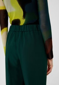 Green trousers with an elastic waistband, made of smooth fabric. Paired with a multicolored patterned long-sleeve top.