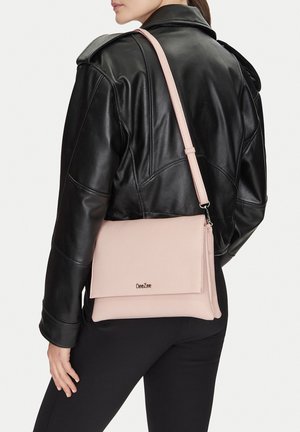 Person trägt schwarze Lederjacke und schwarze Hose, mit einer hellrosa Umhängetasche mit Klappe und "DeeZee"-Logo.